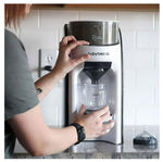 Person using a babybrezza formula dispenser on a kitchen counter.
