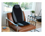 Black and gray massage chair pad on a brown leather chair in a bright room with large windows.