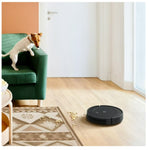 Robotic vacuum cleaner on a wooden floor with a dog on a green couch