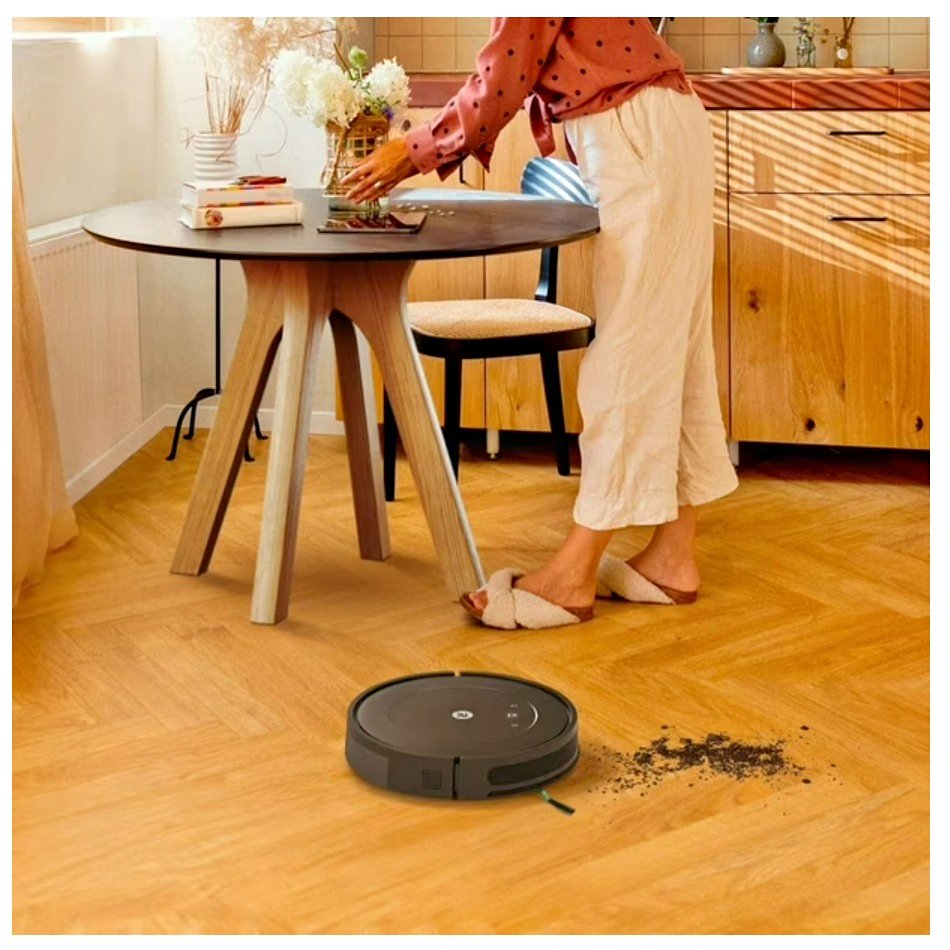 Person using a robot vacuum cleaner on a wooden floor in a kitchen.