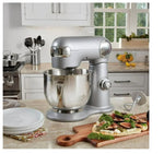Silver stand mixer on a kitchen counter with a pizza and vegetables